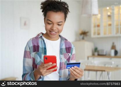 Happy mixed race teen girl holding credit card, shopping on smartphone. Smiling modern young female paying for purchases on internet using mobile bank app, online banking services, standing at home.. Happy mixed race teen girl holding bank credit card, shopping on smartphone. Online banking services