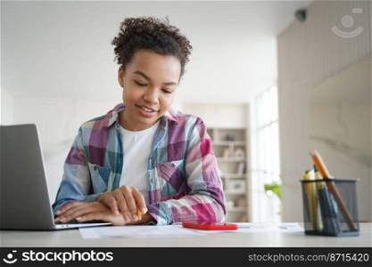 Happy mixed race teen girl student sitting at desk with laptop studying distantly at home. Smiling focused young schoolgirl solves the task, doing homework. Modern distance education concept.. Mixed race teen girl student study sitting at desk with laptop doing homework. Distance education