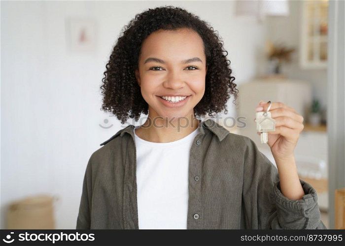 Happy mixed race teen girl tenant showing house key. Friendly smiling young biracial lady renter holding keys to new home apartment, standing in modern flat room. Rental service advertisement.. Keys to new home. Happy mixed race girl tenant shows house apartment key. Rental service advertising