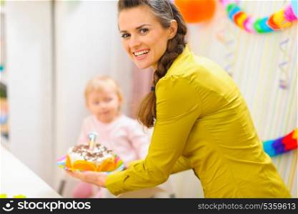 Happy mom carries birthday cake for baby