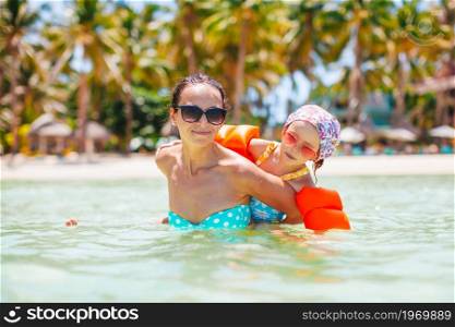 Happy mom with her kid swim in turquoise water in the sea. Young beautiful mother having fun with her daughter on tropical beach vacation