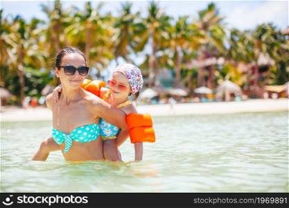 Happy mom with her kid swim in turquoise water in the sea. Young beautiful mother having fun with her daughter on tropical beach vacation