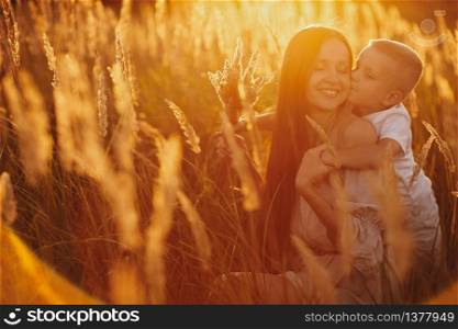 Happy Mom with Her Little Son Enjoying Summer Weekend Outside the City in the Field at Sunny Day Sunset. Young mother playing, hugging, kissing with her little son. Mother&rsquo;s Day. selective focus.. Happy Mom with Her Little Son Enjoying Summer Weekend Outside the City in the Field at Sunny Day Sunset. Young mother playing, hugging, kissing with her little son. Mother&rsquo;s Day. selective focus