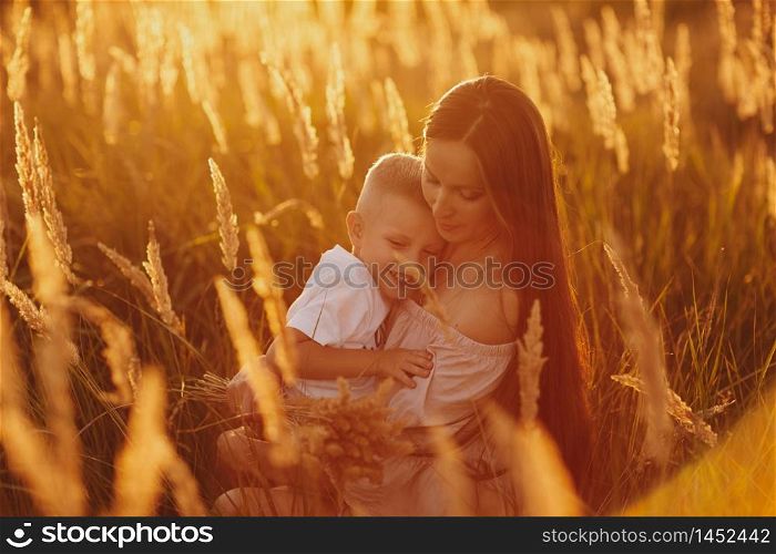 Happy Mom with Her Little Son Enjoying Summer Weekend Outside the City in the Field at Sunny Day Sunset. Young mother playing, hugging, kissing with her little son. Mother&rsquo;s Day. selective focus.. Happy Mom with Her Little Son Enjoying Summer Weekend Outside the City in the Field at Sunny Day Sunset. Young mother playing, hugging, kissing with her little son. Mother&rsquo;s Day. selective focus