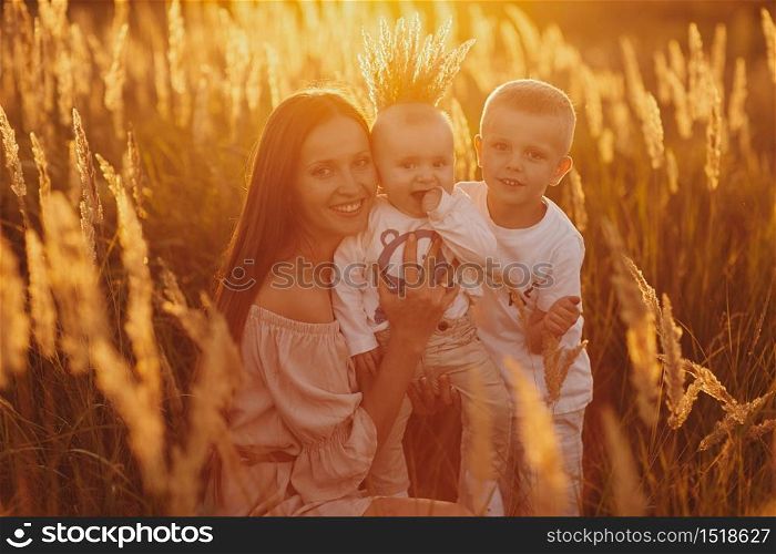 happy mom with her two sons in a field at sunset. happy childhood. A young woman hugs her son.. happy mom with her two sons in a field at sunset. happy childhood. A young woman hugs her son