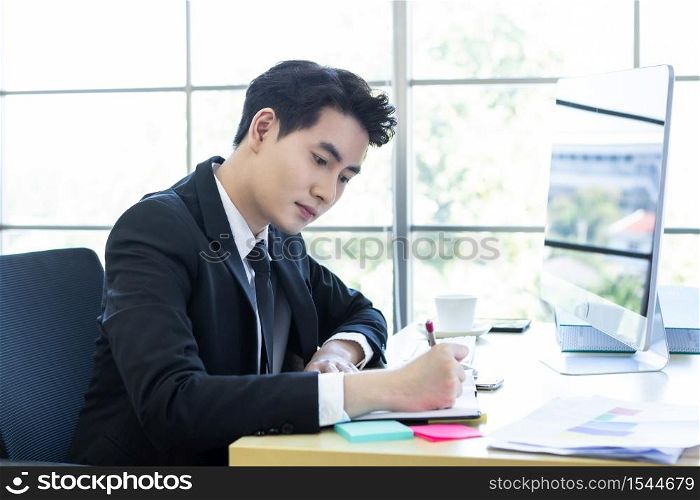 Happy mood a cheerful of asian young businessman have ideas make a note the successful business plan in a notebook and computer on wooden table background in office.