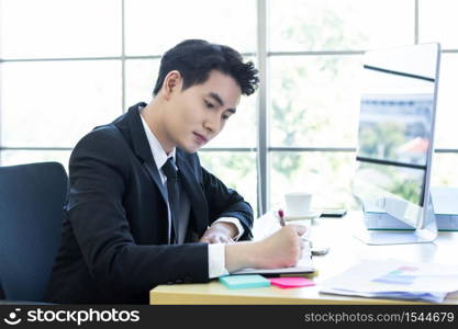 Happy mood a cheerful of asian young businessman have ideas make a note the successful business plan in a notebook and computer on wooden table background in office.