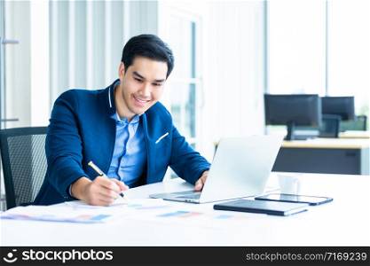 Happy mood a cheerful of asian young businessman have ideas make a note the successful business plan in document paper and laptop computer on wooden table background in office.