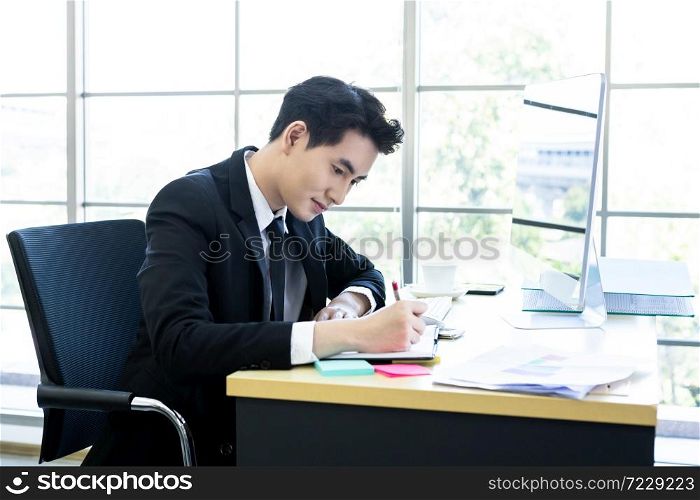 Happy mood a cheerful of asian young businessman have ideas make a note the successful business plan in document paper and computer on wooden table background in office.