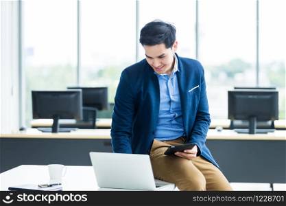 Happy mood asian young businessman working with laptop computer sit on the table In the office room background.