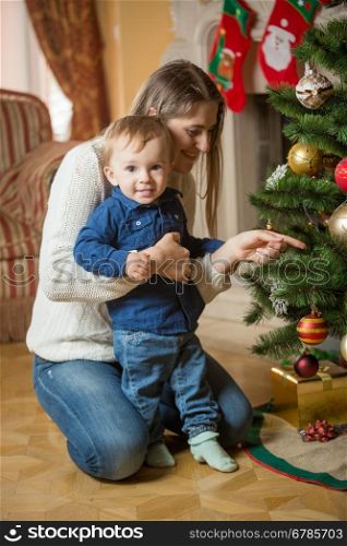 Happy mother and 10 months old baby boy decorating Christmas tree at house