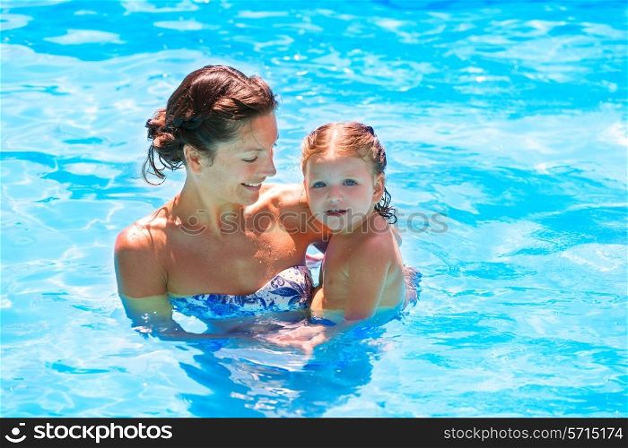 Happy mother and baby daughter at swimming pool in summer vacation