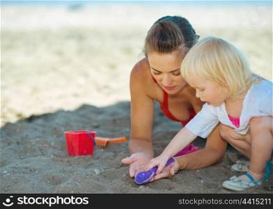 Happy mother and baby girl playing with sand on beach