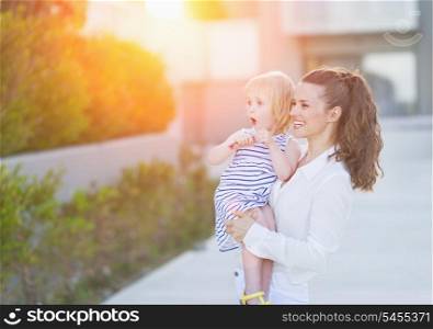 Happy mother and baby in front of house building looking on copy space