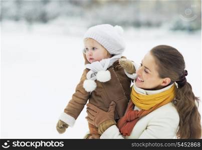 Happy mother and baby looking on copy space in winter outdoors