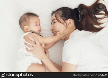 happy mother and baby lying on a bed at home, top view