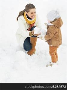 Happy mother and baby making snowman in winter park