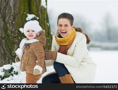 Happy mother and baby playing outdoors in winter