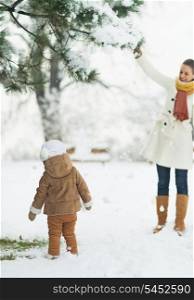 Happy mother and baby playing with snow on branch
