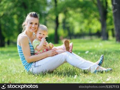 Happy mother and baby sitting on grass in park
