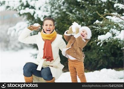 Happy mother and baby throwing snowballs in winter park