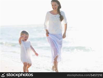 Happy mother and baby walking along sea coast