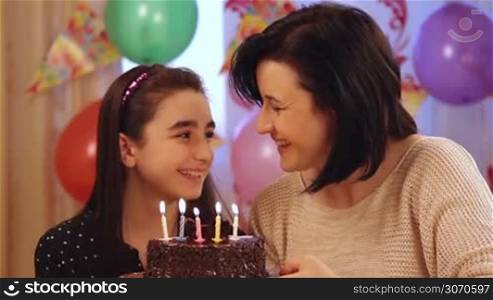 Happy mother and daughter blowing candles of birthday cake