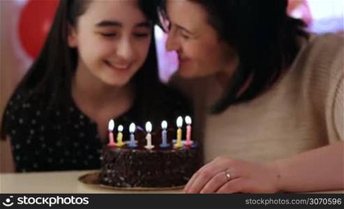 Happy mother and daughter blowing candles on birthday cake