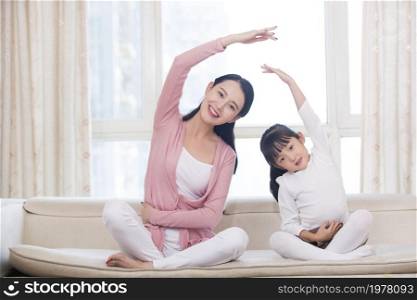 Happy mother and daughter doing yoga at home