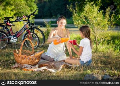 Happy mother and daughter drinking orange juice at picnic