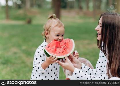 happy mother and daughter eat watermelon in summer park. Happy smiling family eating watermelon in park. Mother and daughter spend time together. Diet, vitamins, healthy food concept. selective focus.. happy mother and daughter eat watermelon in summer park. Happy smiling family eating watermelon in park. Mother and daughter spend time together. Diet, vitamins, healthy food concept. selective focus