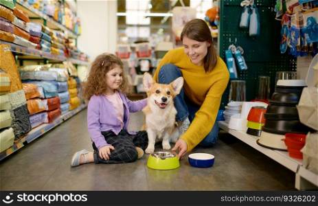 Happy mother and daughter feeding their corgi dog at pet shop. Happy mother and daughter feeding their dog at pet shop