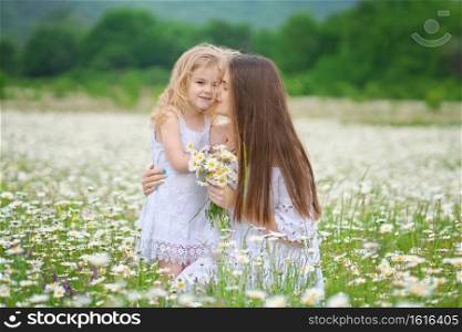 Happy mother and daughter in big camomile mountain meadow. Emotional, love and care scene.