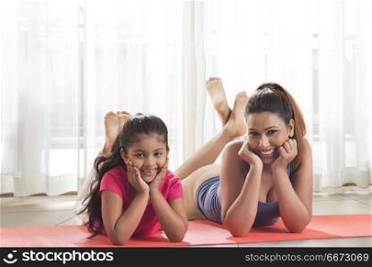 Happy mother and daughter lying on yoga mat