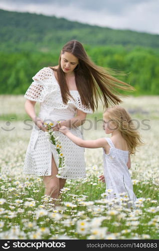 Happy mother and daughter making wreath in big camomile mountain meadow. Emotional, love and care scene.