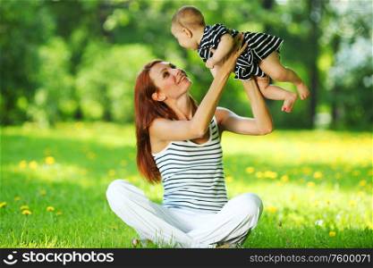 Happy mother and daughter on the green grass in summer park. Mother and daughter on the green grass