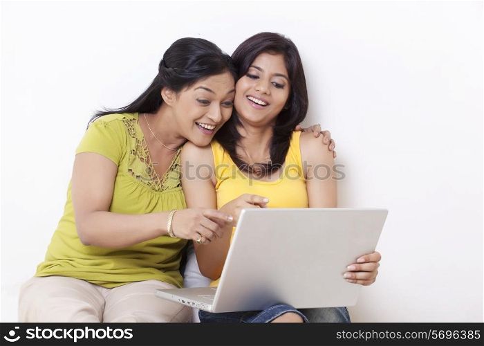 Happy mother and daughter pointing at laptop over white background