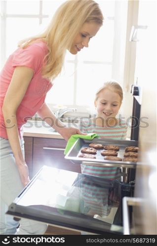 Happy mother and daughter removing cookie tray from oven at home