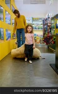 Happy mother and daughter shopping together at pet shop on weekend. Focus on little girl carrying new soft bed pillow for her domestic animal. Happy mother and daughter shopping together at pet shop on weekend