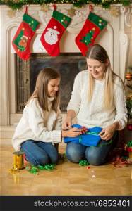 Happy mother and daughter sitting on floor at fireplace and packing sweater for Christmas present