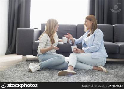 Happy mother and daughter talking while having coffee in living room