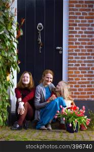 happy mother and daughters sit on the porch of their house