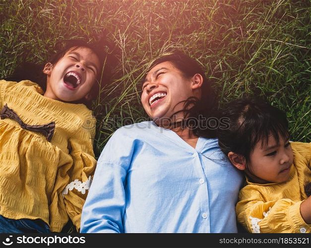 Happy mother and daughters smiling and laughing lying on the lawn in summer park. Family spend their free time together on vacation.