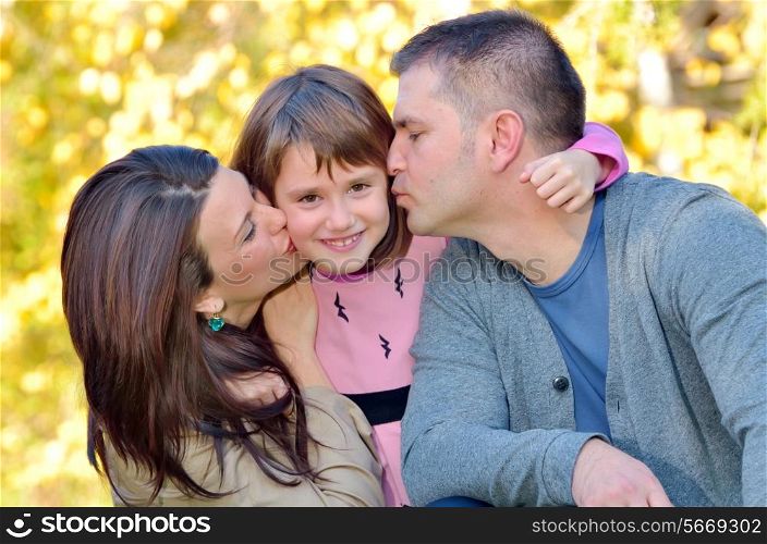 Happy mother and father kissing their daughter in the park
