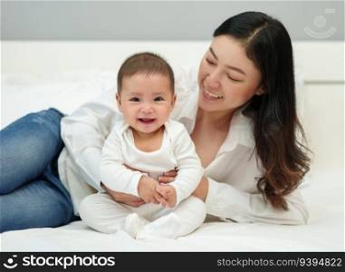 happy mother and her infant baby sitting and playing on a bed