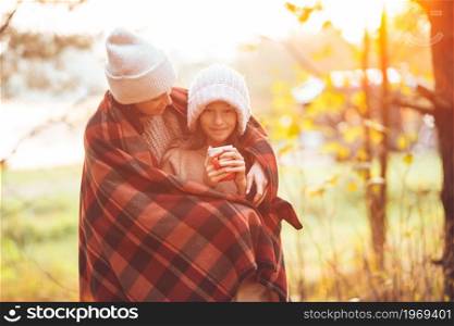 Happy mother and little girl with mug at autumn day wrapped in a blanket. Beautiful family at autumn warm day together