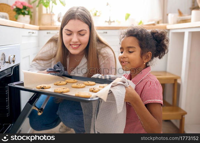 Happy mother and little kid cooking cakes in oven on breakfast. Smiling family on the kitchen in the morning. Mom feeds female child, good relationship. Mother and kid cooking cakes in oven on breakfast