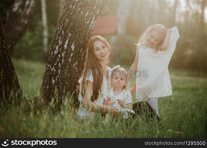 Happy mother and two daughter in the park. Beauty nature scene with family outdoor lifestyle. Happy family resting together on the green grass, having fun outdoor. Happiness and harmony in family life.. Happy mother and two daughter in the park. Beauty nature scene with family outdoor lifestyle. Happy family resting together on the green grass, having fun outdoor.