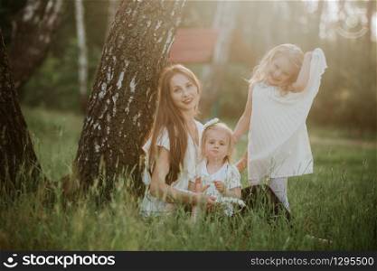 Happy mother and two daughter in the park. Beauty nature scene with family outdoor lifestyle. Happy family resting together on the green grass, having fun outdoor. Happiness and harmony in family life.. Happy mother and two daughter in the park. Beauty nature scene with family outdoor lifestyle. Happy family resting together on the green grass, having fun outdoor.