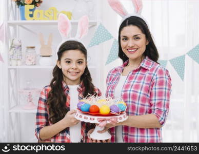 happy mother daughter holding colorful easter eggs nest cakestand